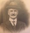 Posed sepia photograph, head and shoulders of Mr. John S. Hearn. Trimed mustache, wearing a hat and white button collar shirt with narrow knotted tie, waistcoat and top coat.
